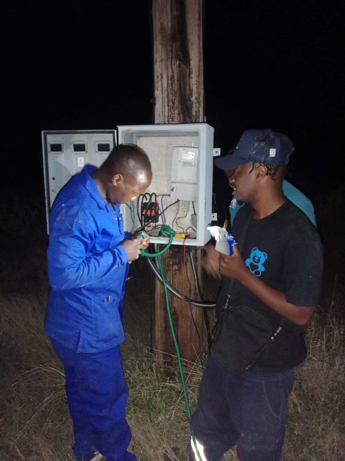 Two technicians working inside an electrical control box